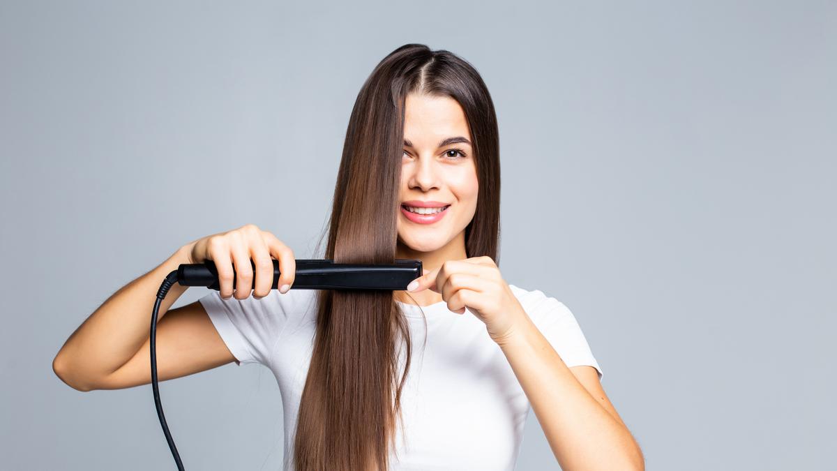 009443600_1759915077-smiling-young-woman-straightening-her-hair-with-white.jpg